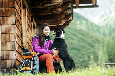 Austria, Altenmarkt-Zauchensee, young woman and dog in front of an Alpin cabin - HHF005115