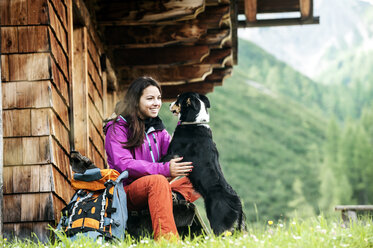 Österreich, Altenmarkt-Zauchensee, junge Frau mit Hund vor einer Alphütte - HHF005115