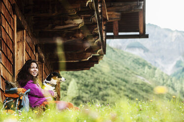 Österreich, Altenmarkt-Zauchensee, junge Frau mit Hund vor einer Alphütte - HHF005116