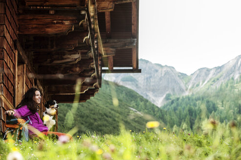 Österreich, Altenmarkt-Zauchensee, junge Frau mit Hund vor einer Alphütte - HHF005117