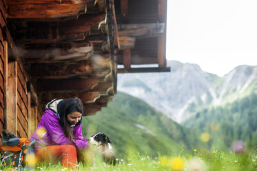 Österreich, Altenmarkt-Zauchensee, junge Frau mit Hund vor einer Alphütte - HHF005119