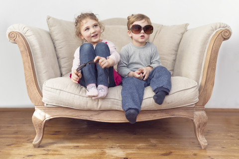 Bruder und Schwester mit übergroßer Sonnenbrille auf der Couch sitzend, lizenzfreies Stockfoto