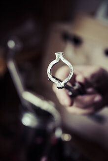 Goldschmied bei der Arbeit an Eheringen im Mokume-Gane-Stil, die Hand hält den unvollendeten Ring - KRPF001295