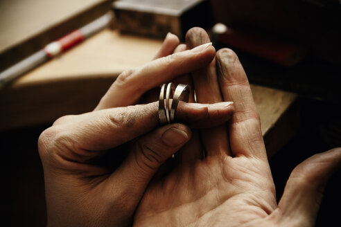 Goldschmied bei der Arbeit an Eheringen, Hand hält unfertigen Ring - KRPF001304