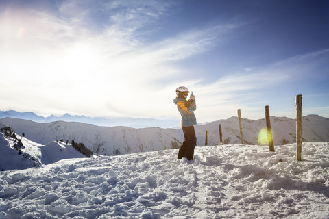 Österreich, Bundesland Salzburg, Region Hochkönig, junge Skifahrerin beim Fotografieren mit Smartphone, lizenzfreies Stockfoto