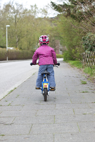 Germany, Kiel, Little girl riding bicycle, rear view stock photo