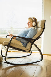 Ältere Frau zu Hause mit Kopfhörern und digitalem Tablet - UUF003477