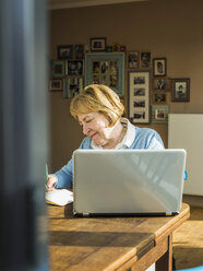 Ältere Frau zu Hause mit Laptop und Notizbuch - UUF003484