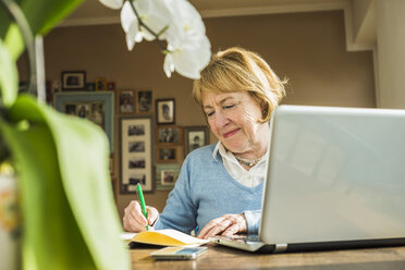 Ältere Frau zu Hause mit Laptop und Notizbuch - UUF003486