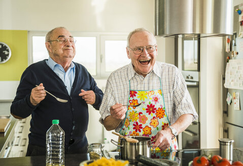 Zwei glückliche ältere Freunde beim Kochen in der Küche - UUF003503