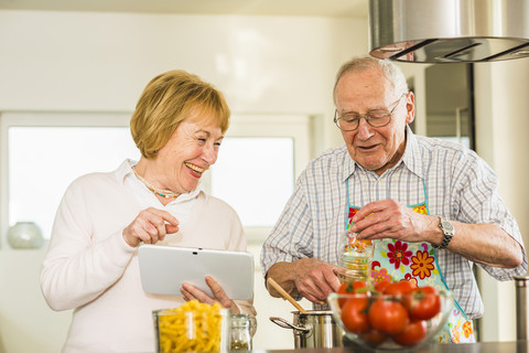 Älteres Paar mit digitalem Tablet beim Kochen in der Küche, lizenzfreies Stockfoto