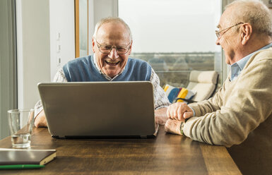 Zwei ältere Freunde schauen auf einen Laptop - UUF003550