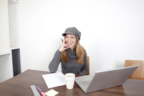 Portrait of smiling woman with laptop sitting at wooden table - PATF000031
