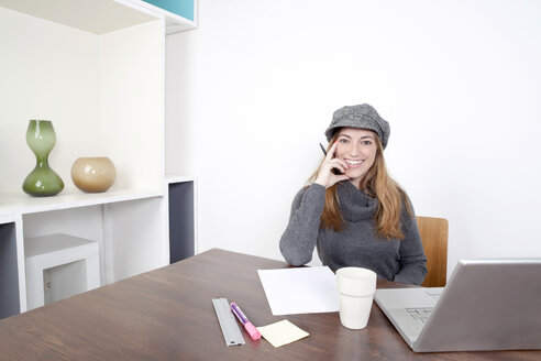 Portrait of smiling woman with laptop sitting at wooden table - PATF000032