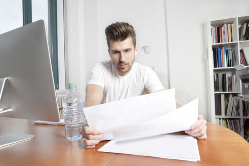 Young man watching documents at desk in an office - PATF000043