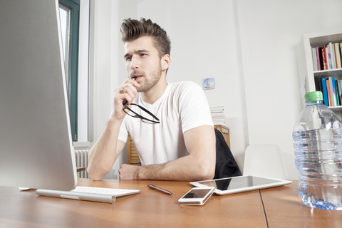 Nachdenklicher junger Mann sitzt am Schreibtisch in einem Büro, lizenzfreies Stockfoto