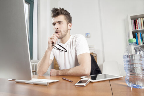 Nachdenklicher junger Mann sitzt am Schreibtisch in einem Büro - PATF000044