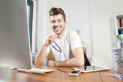Porträt eines lächelnden jungen Mannes am Schreibtisch in einem Büro, lizenzfreies Stockfoto