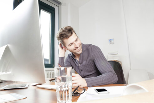 Lächelnder junger Mann am Schreibtisch in einem Büro - PATF000046