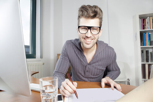 Porträt eines lächelnden jungen Mannes am Schreibtisch in einem Büro - PATF000039