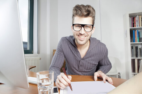 Portrait of smiling young man at desk in an office - PATF000039