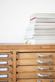 Stapel von Büchern und Zeitschriften auf einem hölzernen Schubladenschrank - PATF000028