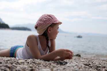 Mädchen mit Mütze am steinigen Strand liegend - SAF000016
