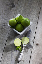 Bowl of limes, sliced lime and knife on wood - CSF024684