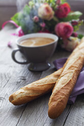 Zwei französische Baguettes, eine Tasse Kaffee, ein Blumenstrauß auf dem Frühstückstisch - CSF024706