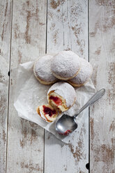 Four Bismarck doughnuts on paper and grey wood - CSF024677