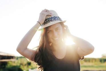 Smiling woman wearing summer hat standing at backlight - BZF000044