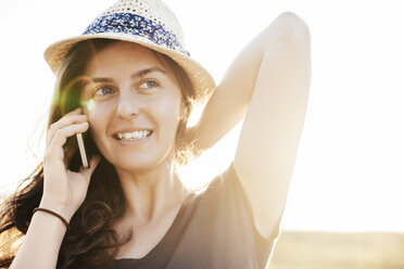 Lächelnde Frau mit Sommerhut, die mit einem Smartphone telefoniert - BZF000050