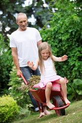 Man pushing his little daughter sitting in a wheelbarrow - WESTF021167