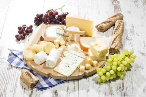 Käseteller mit verschiedenen Käsesorten, Baguette und Weintrauben auf Holz, lizenzfreies Stockfoto