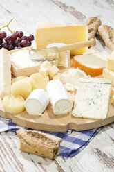 Käseteller mit verschiedenen Käsesorten, Baguette und Weintrauben auf Holz - MAEF009870