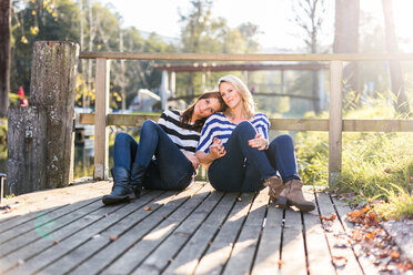 Lesbian couple in love sitting on a jetty - DAWF000255