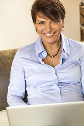 Mature woman sitting on couch using laptop - JFEF000618