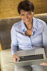 Mature woman sitting on couch using laptop - JFEF000619