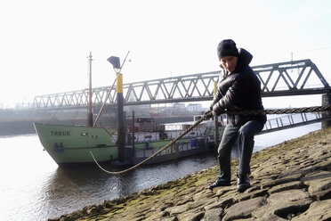 Deutschland, Bremerhaven, Mann zieht Seil von Frachtschiff - NDF000516