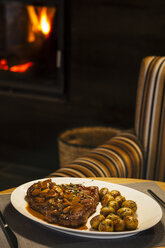 Kalbsschnitzel mit Sauce und Champignons auf Teller, Sessel und Kamin im Hintergrund - AKNF000009