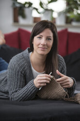 Portrait of smiling woman crocheting on couch - SHKF000265