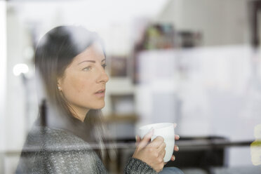 Frau mit Kaffeetasse schaut durch eine Fensterscheibe - SHKF000270