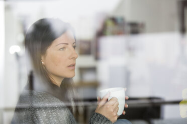 Woman with coffee cup looking through windowpane - SHKF000270