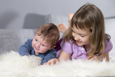 Kleines Mädchen und neugeborener Bruder liegen zusammen auf einem Schafsfell - ROMF000054