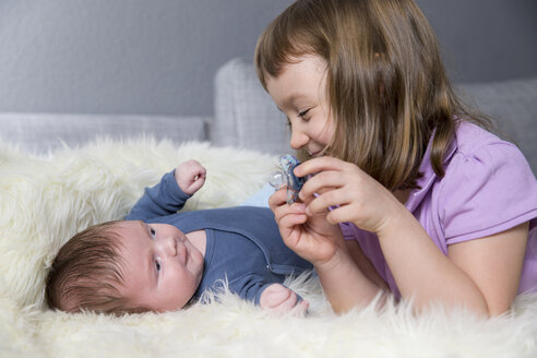 Kleines Mädchen und neugeborener Bruder liegen von Angesicht zu Angesicht auf einem Schafsfell - ROMF000056