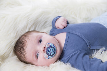 Portrait of newborn baby boy with pacifier lying on sheepskin - ROMF000057