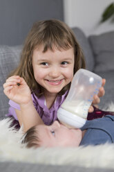 Porträt eines glücklichen kleinen Mädchens, das seinen neugeborenen Bruder mit der Babyflasche füttert - ROMF000059