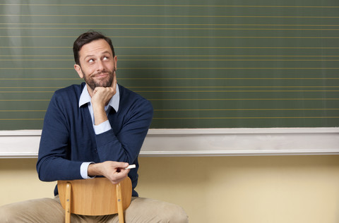 Smiling teacher in classroom at blackboard looking up stock photo