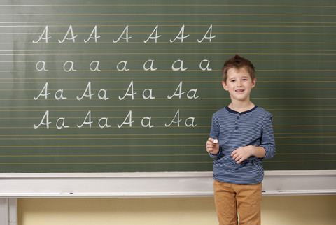 Schuljunge schreibt an der Tafel den Buchstaben A, lizenzfreies Stockfoto