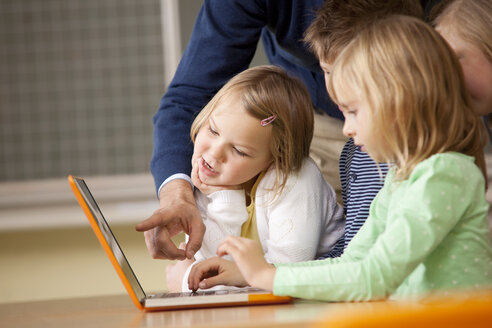 Lehrerin mit Schülern, die einen Laptop im Klassenzimmer benutzen - MFRF000096